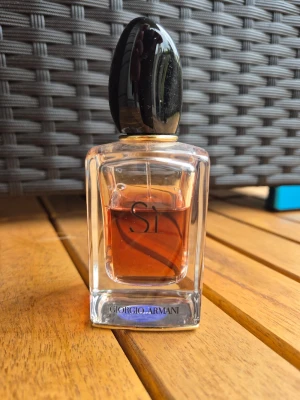 Giorgio Armani Sì parfym - Elegant parfymflaska från Giorgio Armani Sì med genomskinligt glas och svart, glansig kork. Doften har en varm bärnstensfärgad vätska och flaskan har en stilren, modern design med märkets logga i botten. Mer än hälften kvar i flaskan 