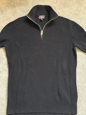Halv zip slim fit - Snygg svart stickad tröja från H&M med halv dragkedja och hög krage. Tröjan har ribbad struktur och är perfekt för lager på lager. Passar till både jeans och chinos för en clean look.