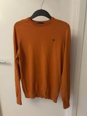 Rostorange långärmad tröja - Snygg rostorange långärmad tröja med rund halsringning och diskret broderad logga på bröstet. Tröjan har ribbade muddar vid ärmslut och nederkant. Perfekt för lager-på-lager och enkel att matcha med jeans eller chinos.