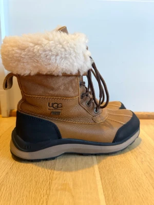 UGG Adirondack vinterstövlar för dam, storlek 37 - Snygga bruna vinterkängor från UGG med varm, fluffig fårskinnskrage och vattentätt läder. Kängorna har snörning framtill, robust sula och svarta detaljer vid hälen och tån. Perfekta för kalla dagar och ger en cool vinterlook.