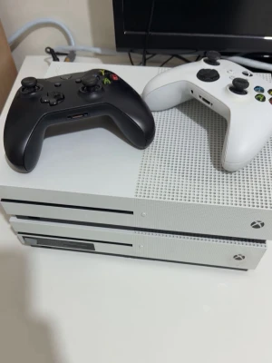 Xbox One S med två handkontroller - Säljer en vit Xbox One S med två trådlösa handkontroller, en svart och en vit. Konsolen har en stilren design med ventilerad ovansida och klassisk Xbox-logga. Perfekt för gaming och streaming.