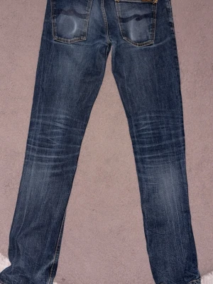 Nudie Jeans Grim Tim - Säljer dessa feta och eftertraktade Nudie jeans för en bra peng! Dom har en unik tvätt och är dry selvedge vilket betyder att tyget har en tendens att bli snyggare ju mer du använder jeansen! Passformen är slim, W32 L36. Hör av dig vid frågor eller funderingar! OBS: Litet hål längst ner på benet som inte syns så bra ✅