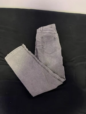 Grå raka jeans med fem fickor - Snygga grå jeans med rak passform och klassisk femficksdesign. Jeansen har bälteshällor och är tillverkade i ett mjukt denimtyg som ger en avslappnad look. Perfekta för dig som gillar en enkel och stilren stil.