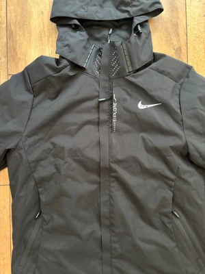 Nike Aeroduct / Explore Vind- & Löparjacka - Svart - Skick som ny 🏃‍♂️💨 - Smidig och funktionell jacka från Nike med "Explore"-detaljer, dragkedjefickor och huva. Perfekt för löprundan, blåsiga dagar eller som snygg vardagsjacka!  Märke: Nike  Färg: Svart  Skick: Mycket fint skick Skickas spårbart eller hämtas enligt överenskommelse. Skicka ett meddelande vid frågor eller om du vill ha fler bilder! 🤝 