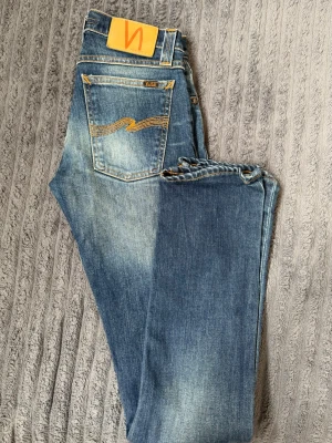 Nudie Jeans Super Slim Kim blå - Säljer ett par blå Super Slim Kim jeans från Nudie Jeans i tvätten Natural Dark. Jeansen har en smal passform, klassiska fem fickor och snygga slitningar. Materialet är 98% bomull och 2% elastan för extra stretch och komfort.