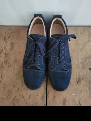 Mörkblåa Christian Louboutin  - Snygga mörkblå sneakers i mocka med klassisk låg profil och matchande mörkblå snören. Skorna har en enkel och stilren design med rund tå och svart sula. Perfekta för dig som gillar en clean och tidlös look.