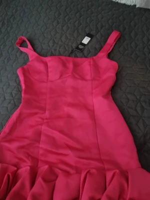 Rosa kort klänning med volang - Supersnygg rosa kort klänning med breda axelband och volangdetaljer nedtill. Klänningen har en figurnära passform och är perfekt för dig som vill sticka ut. Tillverkad i ett slätt material som ger en lyxig känsla. Oanvänd storlek S men den passar M också. 