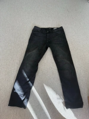 Svarta jeans från Jack & Jones - Snygga svarta jeans från Jack & Jones i modellen Regular Clark. Klassisk femficksdesign, raka ben och normal midja. Jeansen har en diskret tvättad look och är tillverkade i ett mjukt bomullsmaterial med lite stretch för extra komfort.