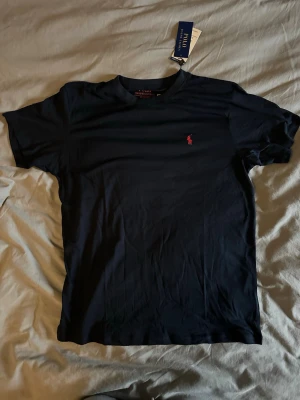 Mörkblå Polo Ralph Lauren T-shirt - En helt ny bomulls tisha i strlk M. Fin kvalitet och logga i rött tryck.
