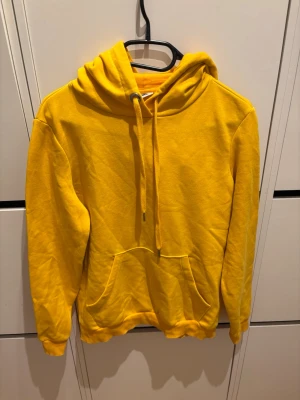 Gul hoodie från Noisy May - Gul hoodie från Noisy May med klassisk känguruficka och dragsko i huvan. Mjuk insida och ribbade muddar vid ärmslut och nederkant. Perfekt för en färgstark och chill stil.