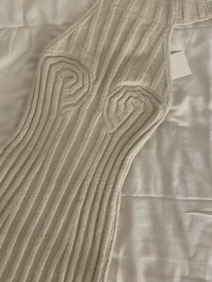 Ribbad stickad klänning från Adoore - Supersnygg ribbad stickad klänning från Adoore i ljusbeige färg. Klänningen har markerade detaljer vid bysten och en kroppsnära passform. Perfekt för dig som gillar trendiga och unika plagg.