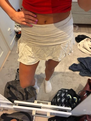 Beige kortkjol med volang - Säljer en beige kortkjol med volangkant och lätt rynkad midja. Kjolen har en mjuk och flowy känsla, perfekt för varmare dagar. Passformen är normal och kjolen har en feminin och trendig look.