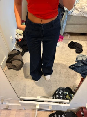 Mörkblå raka jeans - Säljer ett par mörkblå jeans med rak passform och hög midja. Jeansen har klassisk femficksdesign och stängs med dragkedja och knapp. Materialet är kraftigt denim som ger en snygg siluett. Perfekta till en avslappnad och trendig look.