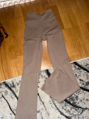 Beiga utsvängda träningstights - Säljer ett par beiga träningstights med hög midja och utsvängda ben. Tightsen har scrunch-detalj bak och är tillverkade i ett stretchigt, mjukt material som passar perfekt för gym eller yoga.