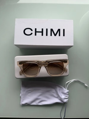 Beige solglasögon från CHIMI - Snygga solglasögon från CHIMI med transparent beige båge och bruna tonade glas. Rektangulär form som ger en modern vibe. Kommer med originalfodral och tygpåse. Perfekta för att lyfta din stil i solen. 