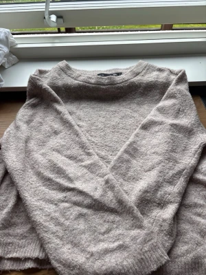Beige stickad tröja med rund hals - Mysig beige stickad tröja med rund halsringning och långa ärmar. Tröjan har en enkel, klassisk design med ribbade muddar vid ärmslut och nederkant. Perfekt för lager på lager och chill dagar.