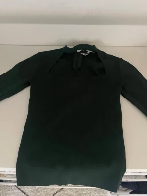 Mörkgrön ribbad klänning från Zara - Snygg mörkgrön ribbad topp från Zara med lång ärm och unik hals. Toppen  är figurnära i modellen. Perfekt att styla med jeans eller kjol för en trendig look.