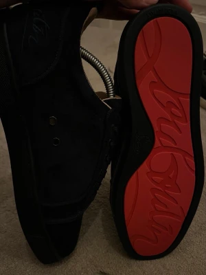 Svarta sneakers med röd sula - Snygga svarta sneakers i mocka med klassisk låg profil och rund tå. Skorna har svarta skosnören och en ikonisk röd yttersula med mönster. Insidan är beige och materialet ser lyxigt ut, perfekt för dig som vill sticka ut.Priset går att diskutera vid snabb affär, finn de frågor så är de bara o skriv 😊