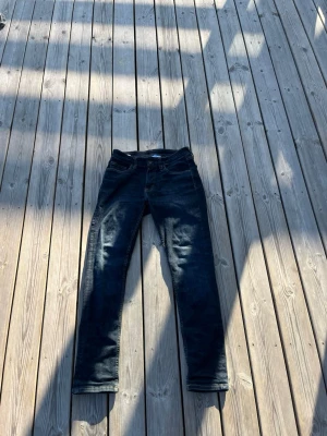 Mörkblå raka jeans - Säljer ett par mörkblå jeans med rak passform och klassisk femficksdesign. Jeansen har subtila slitningar och kontrastsömmar, perfekta för en avslappnad och stilren look. Materialet är denim med lätt stretch för extra komfort.