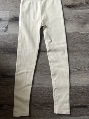 Beige ribbade mjukisbyxor - Snygga beige leggings med ribbad struktur och hög midja. De är stretchiga och har en smal passform som sitter tajt längs benen. Perfekta att matcha med en oversized hoodie eller crop top för en chill look. Eller att träna i. 