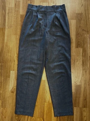 Grå, rutiga kostymbyxor från Cubus - Storlek 36 - Säljer ett par snygga kostymbyxor från Cubus! Perfekta både till jobbet eller till en mer uppklädd vardagslook! Storlek: 36. Färg: Grå. Mönster: Rutiga. Knäpps med knapp och dragkedja. Två djupa framfickor. Material: 62 % Polyester, 33 % Viskos och 5 % Elastan. Foder: 100 % Polyester. Säljs i bra skick! Kika gärna in på mina andra annonser, jag säljer just nu flera klädesplagg! Hör av dig vid frågor och intresse!