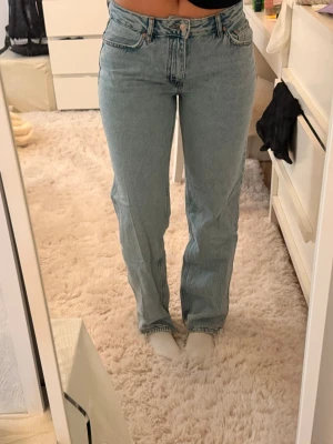 Ljusblå raka jeans med hög midja - Säljer ett par ljusblå jeans med rak passform och hög midja. Klassisk femficksmodell med knapp och dragkedja framtill. Jeansen har en tidlös look och är tillverkade i ett denimtyg som känns mjukt men ändå robust.