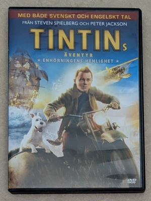 Tintins äventyr: Enhörningens hemlighet , DVD - HELT OANVÄND DVD. Spännande äventyrsfilm om Tintin och hans hund Milou som ger sig ut på jakt efter en gömd skatt. Omslaget är färgstarkt med blå och gula toner, och visar Tintin på motorcykel. DVD-fodral i plast med svensk och engelsk tal.