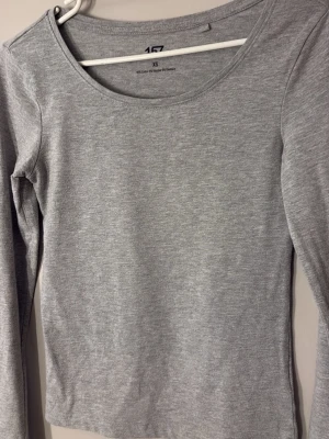 Grå långärmad topp i bomull - En basic grå långärmad topp med rund halsringning. Tillverkad i mjuk bomull, perfekt att styla med jeans eller kjol. Enkel och stilren design som funkar till många olika looks.