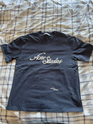 Mörblå Acne Studios t-shirt - Säljer en stilren och klassisk t-shirt från svenska lyxmärket Acne Studios. T-shirten har en snygg blekt svart/mörkgrå nyans som ger en tidlös vintagekänsla. Den har en broderad Acne Studios-logga i vitt på bröstet samt en mindre broderad logga nedtill.  • Märke: Acne Studios • Storlek: M • Skick: Som ny • Färg: Mörkblå med vitt broderi  En exklusiv t-shirt i hög kvalitet med den minimalistiska Acne-estetiken.  Skickas snabbt och spårbart. Hör gärna av dig om du har några frågor!