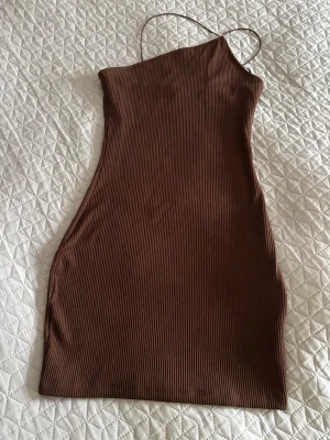 Brun ribbad one shoulder klänning - Säljer en brun, ribbad kortklänning med one shoulder och smala axelband. Klänningen har en tight passform och är perfekt för dig som gillar en enkel men trendig stil. Materialet känns mjukt och följsamt mot kroppen.