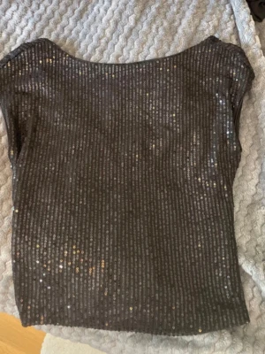 Svart paljettopp med rund hals - Snygg svart topp täckt med glittriga paljetter och rundad halsringning. Toppen är ärmlös och har en croppad passform som ger en trendig look. Perfekt för dig som vill sticka ut och glänsa lite extra.