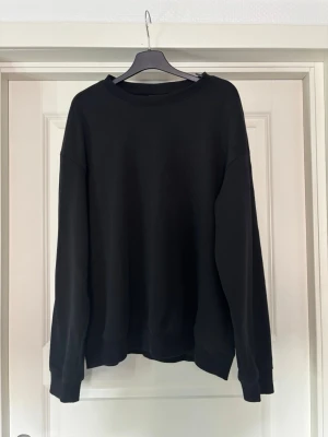 Svart loose fit hoodie från H&M - En svart hoodie från H&M i loose fit-modell. Tröjan har rund halsringning, långa ärmar och ribbade muddar vid ärmslut och nederkant. Perfekt för en avslappnad och stilren look.