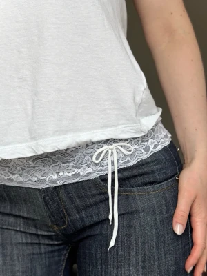 Vitt spetsbälte med rosett - Säljer ett vitt bälte i spets med dekorativ rosett framtill. Bältet har ett romantiskt och feminint uttryck med blommigt spetsmönster och smal knytning. Perfekt för att ge en extra touch till jeans eller kjol. 🌟🌟🌷