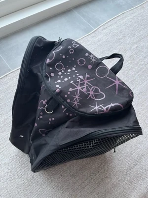Konståknings väska - Cool svart ryggsäck med lila och vita grafiska mönster av cirklar och stjärnor. Ryggsäcken har ett stort huvudfack, dragkedja, nätficka på sidan och praktiskt bärhandtag. Tillverkad i slitstarkt tygmaterial och passar perfekt för skola eller utflykter.