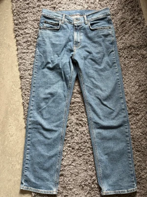 Blå raka jeans från Dressmann - Klassiska blå jeans från Dressmann med rak passform och fem fickor. Jeansen har en ljus tvätt och detaljerade sömmar. Tillverkade i slitstark denim med läderpatch bak i midjan. Perfekta för en avslappnad och tidlös stil.
