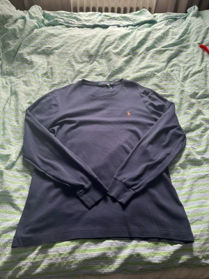 Mörkblå långärmad tröja Polo Ralph Lauren - Snygg mörkblå långärmad tröja från Polo Ralph Lauren som funkar med L, i modellen Custom Slim Fit. Tröjan har rund halsringning och den klassiska broderade loggan i gult på bröstet. Tillverkad i mjuk bomull för en bekväm känsla.