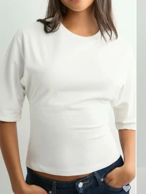 Vit croppad topp med knyt i ryggen från Nelly  - Säljer en vit croppad topp med halvlånga ärmar och snygg öppen rygg med breda band som knyts i en rosett. Toppen har en enkel, clean look och är gjord i mjuk bomull. Perfekt för dig som vill ha en trendig och bekväm stil.