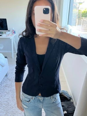  figursydd kavaj med  knappar - Snygg marinblå kavaj med figurnära passform och två knappar från märket Zero!! Kavajen har klassisk krage och trekvartsärmar. Perfekt att styla till jeans eller kjol för en trendig look.