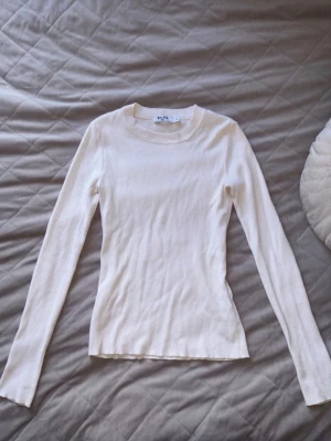 Vit långärmad ribbad tröja - Slimmad vit långärmad tröja med rund halsringning och ribbad struktur. Perfekt basplagg som är lätt att matcha till olika outfits. Materialet ser mjukt och stretchigt ut för en bekväm passform.