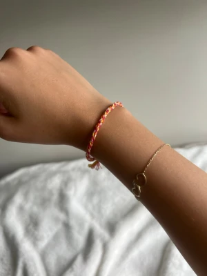 Färgglatt flätat vänskapsarmband - Säljer ett handgjort vänskapsarmband i flätad design med rosa, gult och orange garn. Armbandet har knytning och är justerbar. Perfekt för dig som gillar färgglada accessoarer och vill ha något personligt på handleden.💕