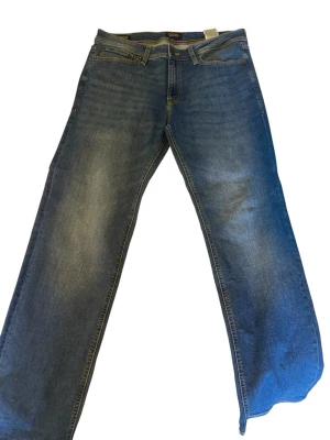 Blå raka jeans från Jack & Jones - Snygga blå jeans från Jack & Jones med klassisk femficksmodell och raka ben. Jeansen har normal midja och är gjorda i slitstarkt denimtyg med subtila slitningar för en avslappnad look. Perfekta till en casual stil.