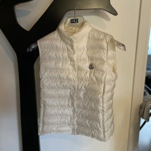 Moncler väst - En vit Moncler väst som precis varit i kemtvätt så den är 10/10, jag säljer den för den är för liten nu för mig, den är i topp skick och fungerar både för killar och tjejer, jag själv är kille men det är en tjej väst men märker inte skillnad, storlek S/1