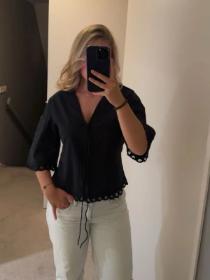 Svart blus med spetsdetaljer - Snygg svart blus från By Malene Birger med v-ringning och knytband framtill. Blusen har trekvartsärm och fina volanger längs ärmslut och nederkant. Blusen är aldrig använd och har därför lappen kvar. Ordenare pris 1800kr 💕💕