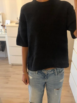 Svart stickad tröja från Gina Tricot - Svart stickad tröja från Gina Tricot med halvlånga ärmar och rund halsringning. Tröjan har en rak passform.