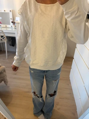 Vit sweatshirt med volang från Springfield - Säljer en vit sweatshirt från Springfield med snygga volangdetaljer längs sidorna och diskret hålmönster framtill. Tröjan har rund halsringning och långa ärmar. 
