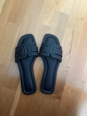 Svarta sandaler med vita sömmar - Stilrena svarta sandaler med fyrkantig tå och breda remmar. Dekorativa vita kontrastsömmar ger en modern touch. Nyskick!