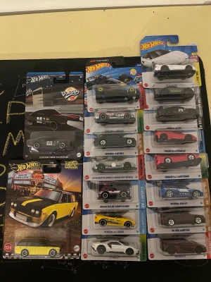 Hot Wheels samling bilar i förpackning - Säljer en samling Hot Wheels bilar i originalförpackning. Blandade modeller som Custom Ford Maverick, Nissan Skyline, Ferrari och fler. Flera färger som svart, gul, vit, röd och blå. Perfekt för samlare eller bilentusiaster som gillar detaljerade miniatyrbilar.