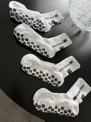 Vita fotbollsstrumpor med grepp - Fyra par vita strumpor med svarta gummidetaljer under foten och texten 'FS FOOTBALL SOCKS' på skaftet. Strumporna är ribbade upptill och har en sportig look, perfekta för träning eller vardag. Materialet är mjukt och stretchigt. Oanvända helt nya