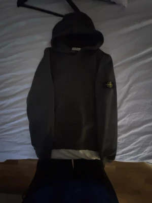 Mörkgrå hoodie från Stone Island - Säljer en mörkgrå hoodie från Stone Island Junior med klassisk huva och den ikoniska logotypen på vänster ärm. Hoodien är tillverkad i mjukt bomullsmaterial och har en avslappnad passform. Perfekt för dig som gillar streetwear och vill ha en stilren look.