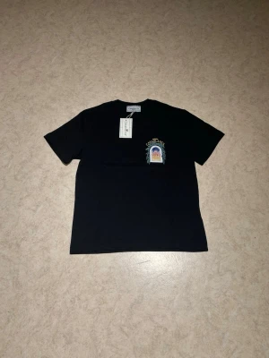 Svart t-shirt från Casablanca - Svart t-shirt från Casablanca med tryck på bröstet i färgglada toner och texten 'Casablanca'. Klassisk rund hals och korta ärmar. Perfekt för dig som vill ha en stilren men ändå unik look.